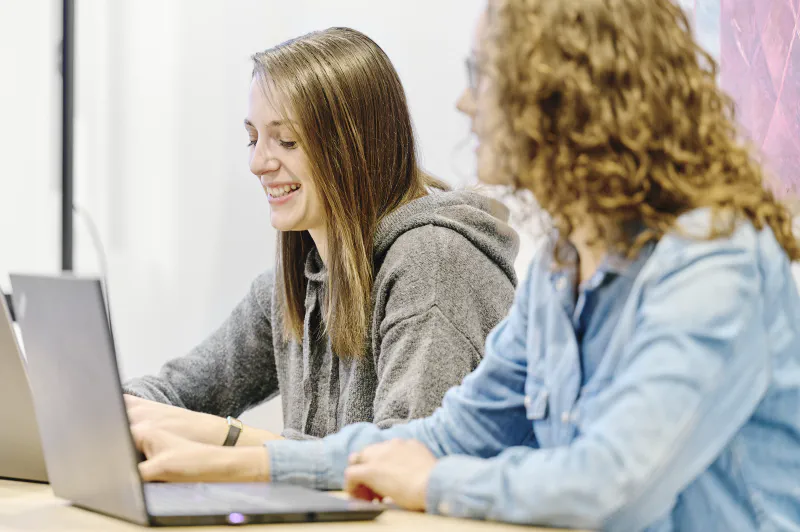 Kolleginnen arbeiten gemeinsam an Laptops