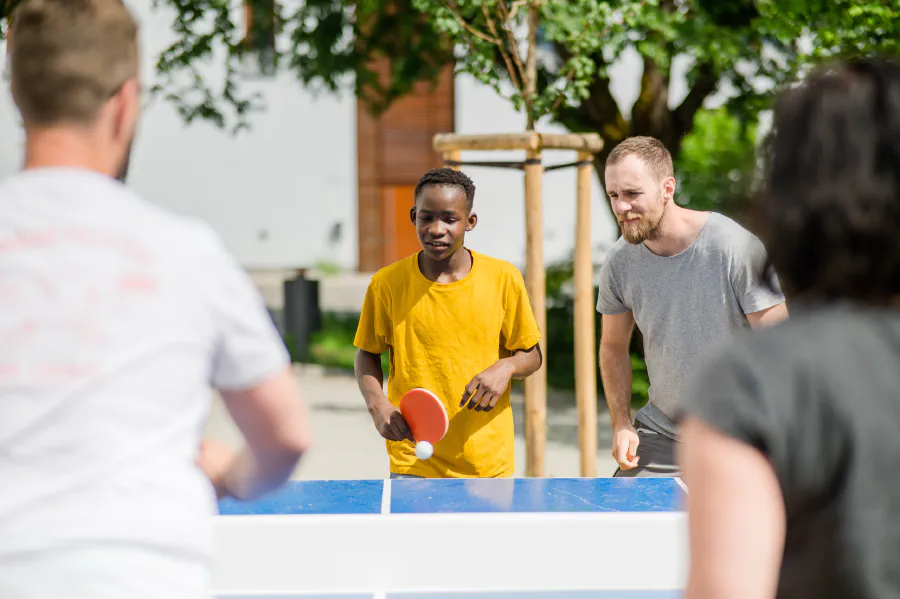 Ein Mitarbeiter spielt gemeinsam mit Jugendlichen einer Ausbildungsstätte Tischtennis.