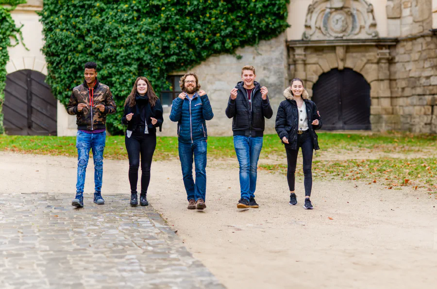 Fünf Menschen der Rummelsberger Diakonie gehen gemeinsam lachend über ein Klostergelände.